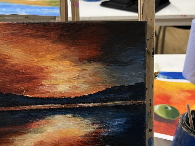 Acrylic painting of a glowing orange sunset over water on an easel