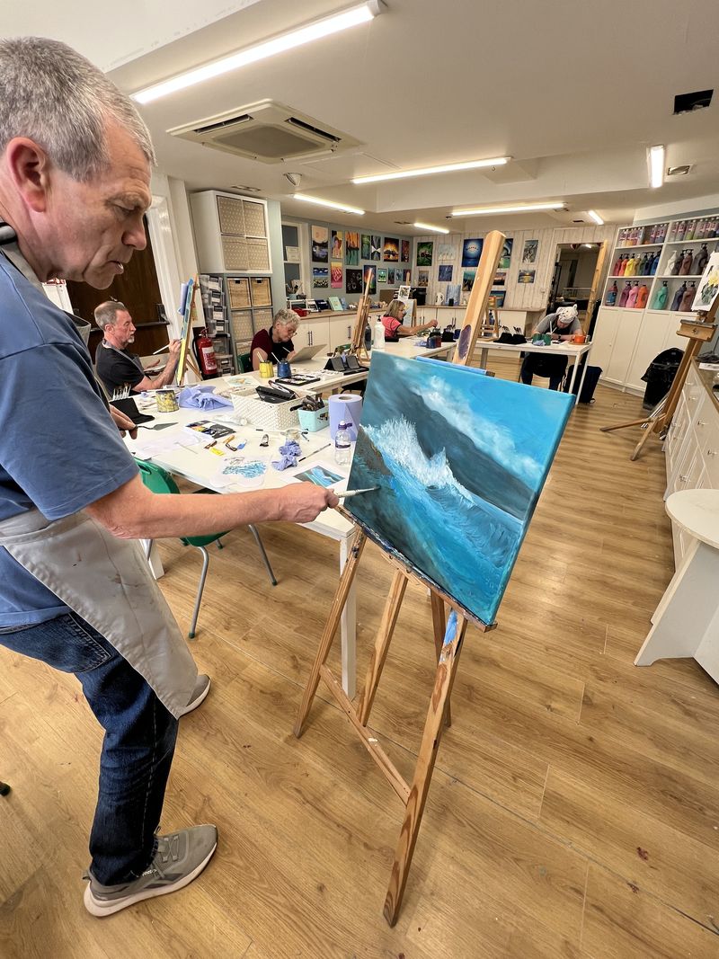 Adult student painting a stormy seascape at an easel during a daytime class