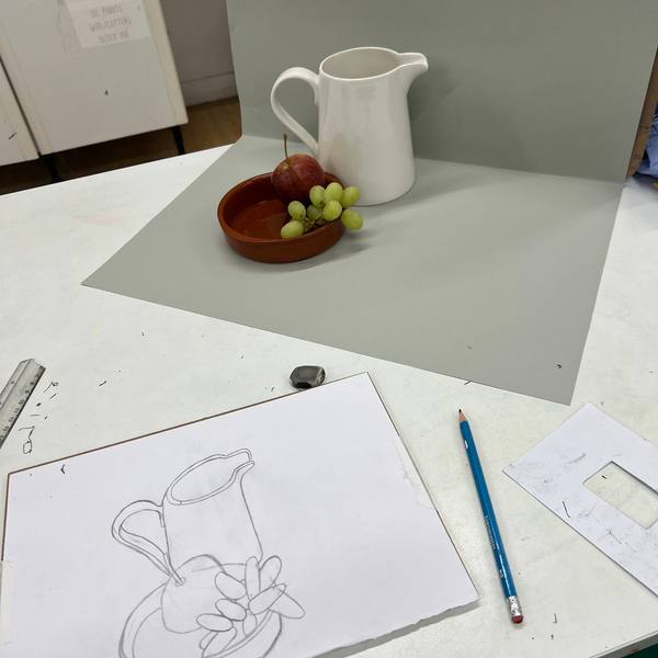 A still life set-up with a jug and an apple beside a student’s drawing