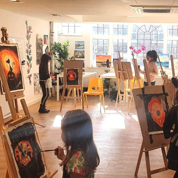 Children painting Halloween pictures at easels in the bright Art School studio during a holiday art camp