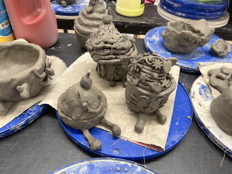Hand-built clay pots and creatures drying on a workshop table