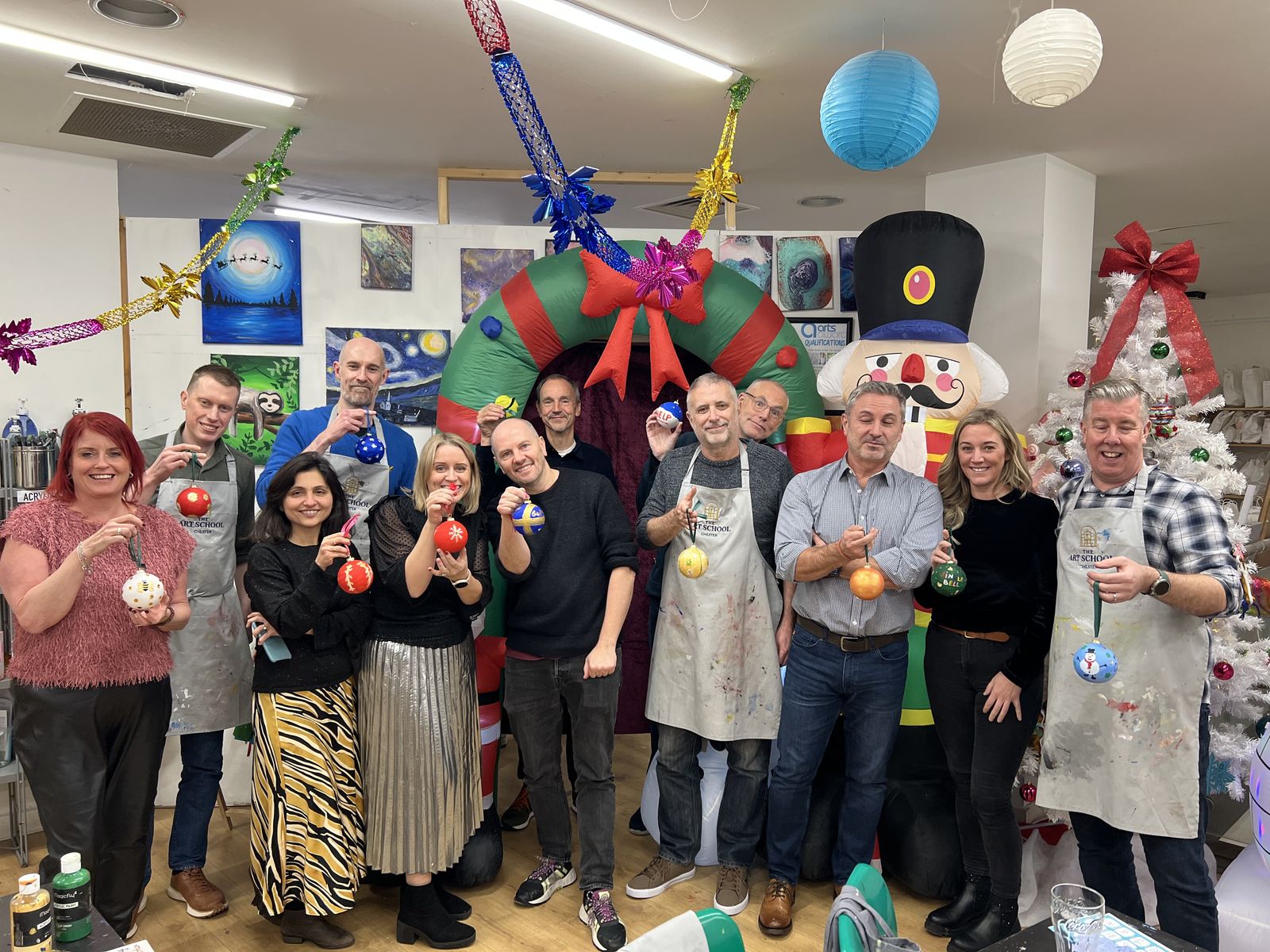 A work team in aprons holding up the Christmas baubles they painted at their team event